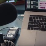 A condenser microphone beside a laptop on a desk in a home recording setup