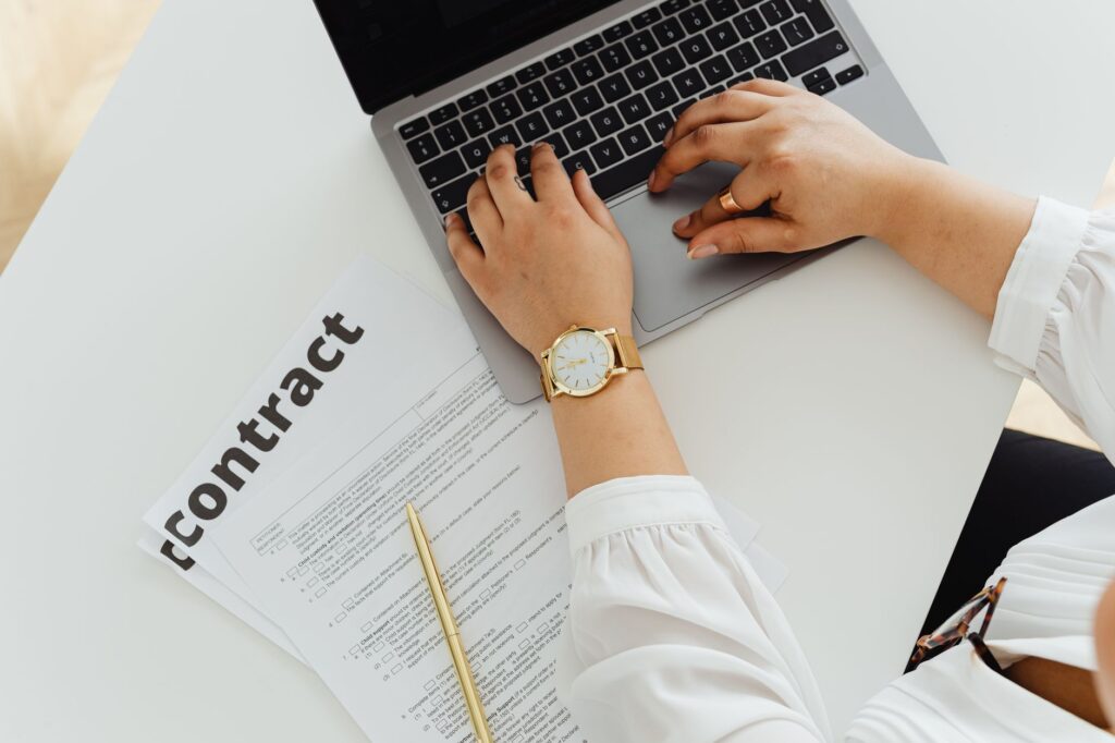 A person reviewing a contract document beside a laptop on a desk during a remote signing session