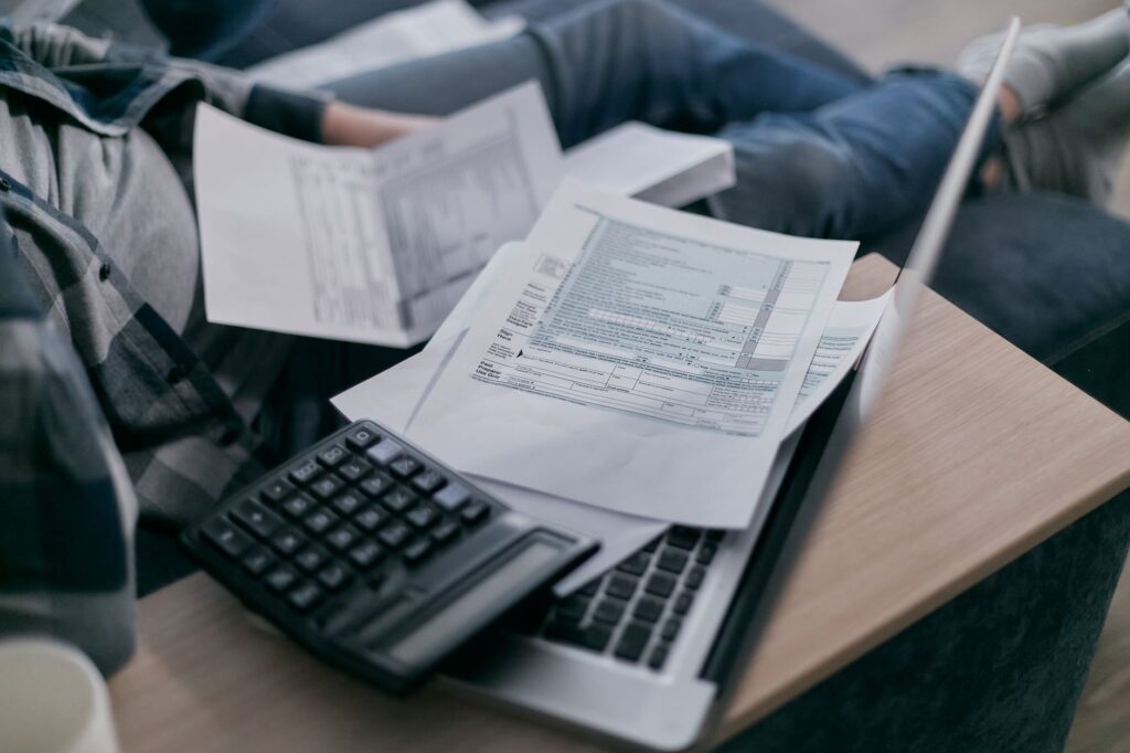 A person at home using a calculator and laptop to work out business finances