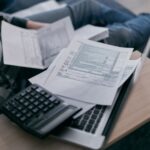 A person at home using a calculator and laptop to work out business finances