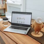 A contemporary office desk setup featuring a laptop, coffee cup, and wooden figurine on a wooden table.